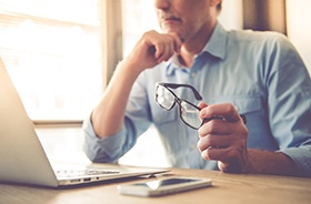 Man in front of computer, researching cost of dentures