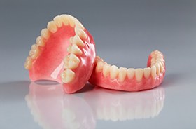 Full upper and lower dentures sitting on reflective surface