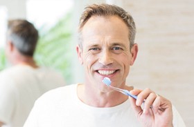 Mature man in white shirt brushing teeth to maintain oral hygiene