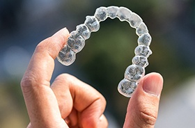 Close-up of hand holding Invisalign aligner between two fingers