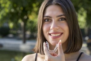 Smiling, dark-haired woman holding aligner for Invisalign treatment