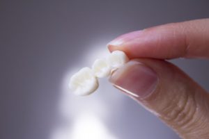 A dental bridge that fell out, held between fingertips