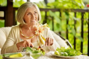 Senior woman enjoying salad with help of implant dentures in Woodbridge