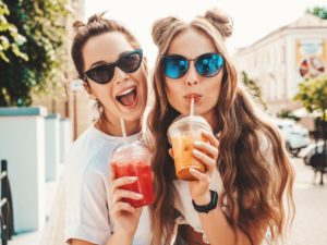 Two friends using straws to enjoy summer beverages